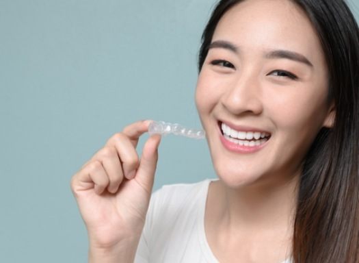 Smiling young woman holding Invisalign aligner