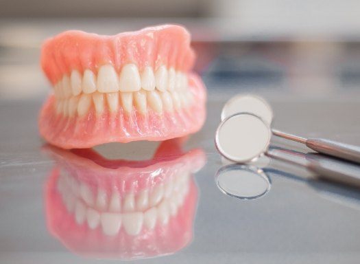Set of full dentures resting next to two dental mirrors