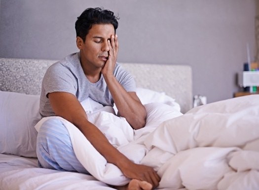 Man sitting up in bed with his hand over his face