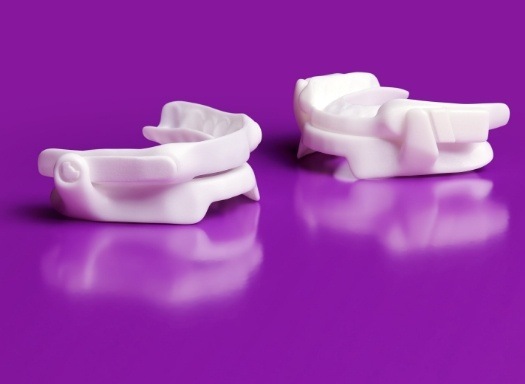 Two white oral appliances against purple background