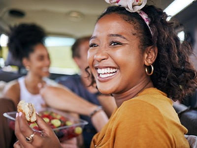 Woman smiling while eating meal with friends in car